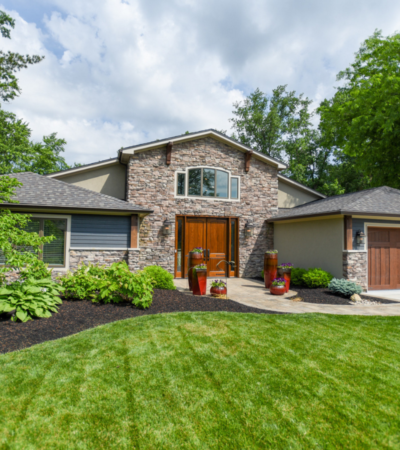 Custom home exterior with stone façade, wood double doors, and landscaped front yard by Build Dayton.