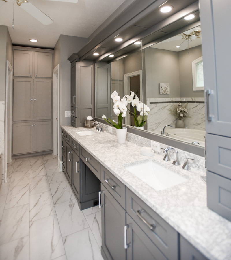 Modern bathroom with gray double vanity, marble countertops, large mirrors, and built-in cabinetry.