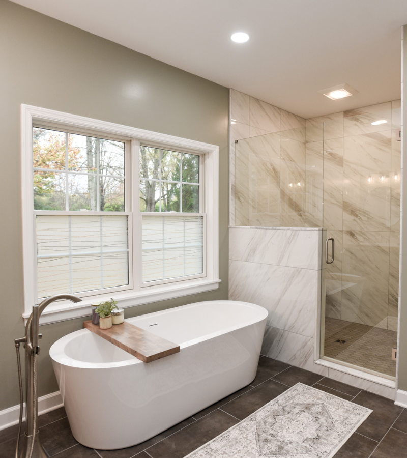 Modern bathroom with freestanding soaking tub, glass-enclosed marble shower, and large window.